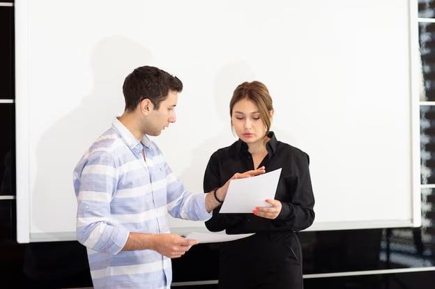 Two business professionals reviewing a report standing in front of a whiteboard in meeting room.