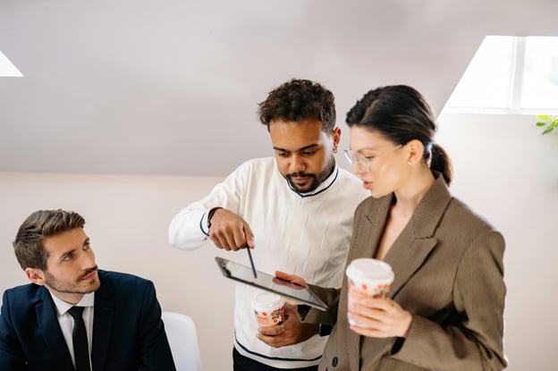 Business professionals in sales meeting with one man sitting and a man and woman standing looking at ipad.