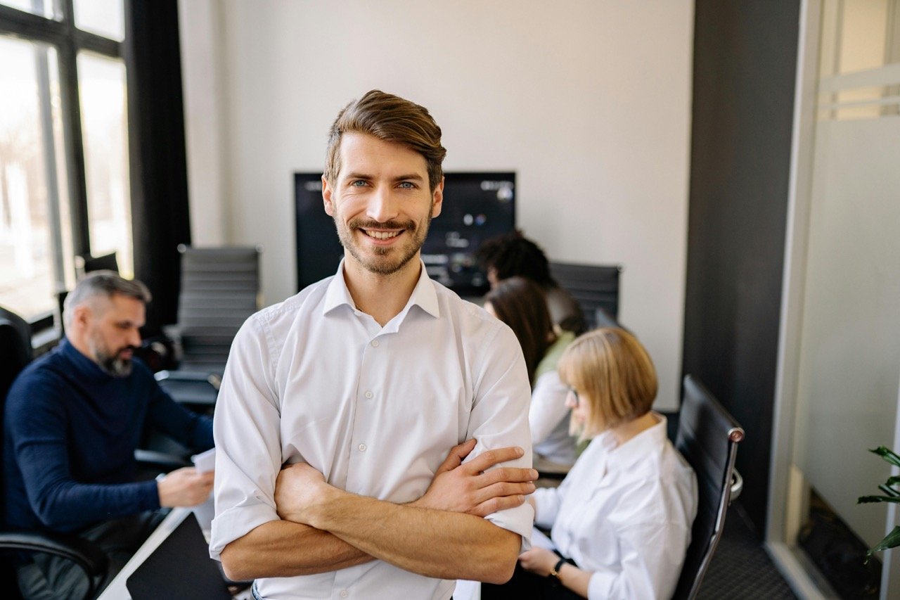 Business professionals in meeting room in modern office space with business man front and centered looking at camera.